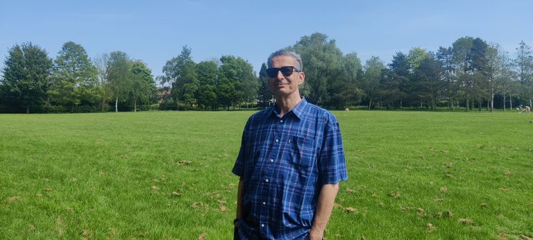 man in blue shirt, with stand of trees in leaf, in the background